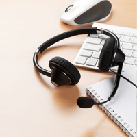 Black headset with microphone on desk beside keyboard, mouse, and notebook on a light wood surface