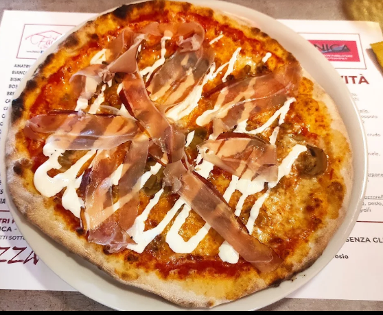Pizza condita con salsa bianca e straccetti di carne su un piatto, vista dall'alto.