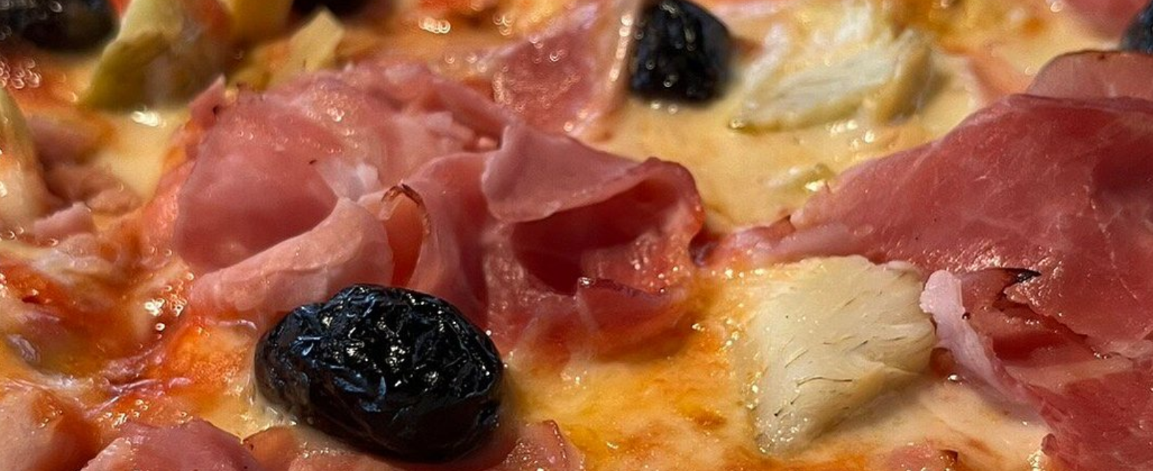 Primo piano di una pizza condita con olive nere e fette di prosciutto ripiegate.