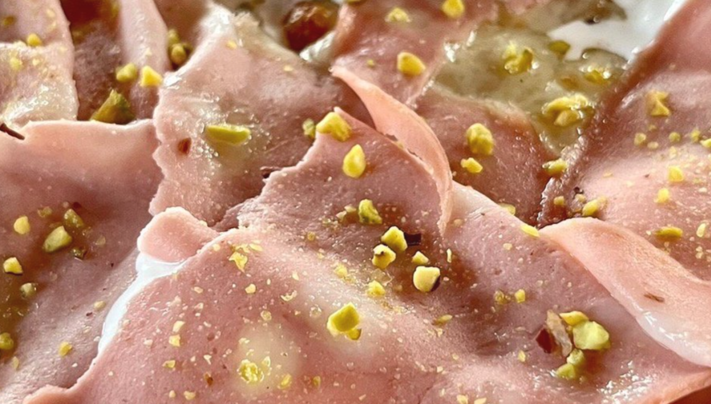 Affettati rosa piegati e guarniti con pistacchi o noci tritate su un piatto