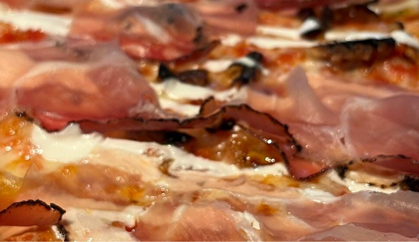 Primo piano di una pizza condita con formaggio fuso, pancetta e pezzi di crosta dorata.