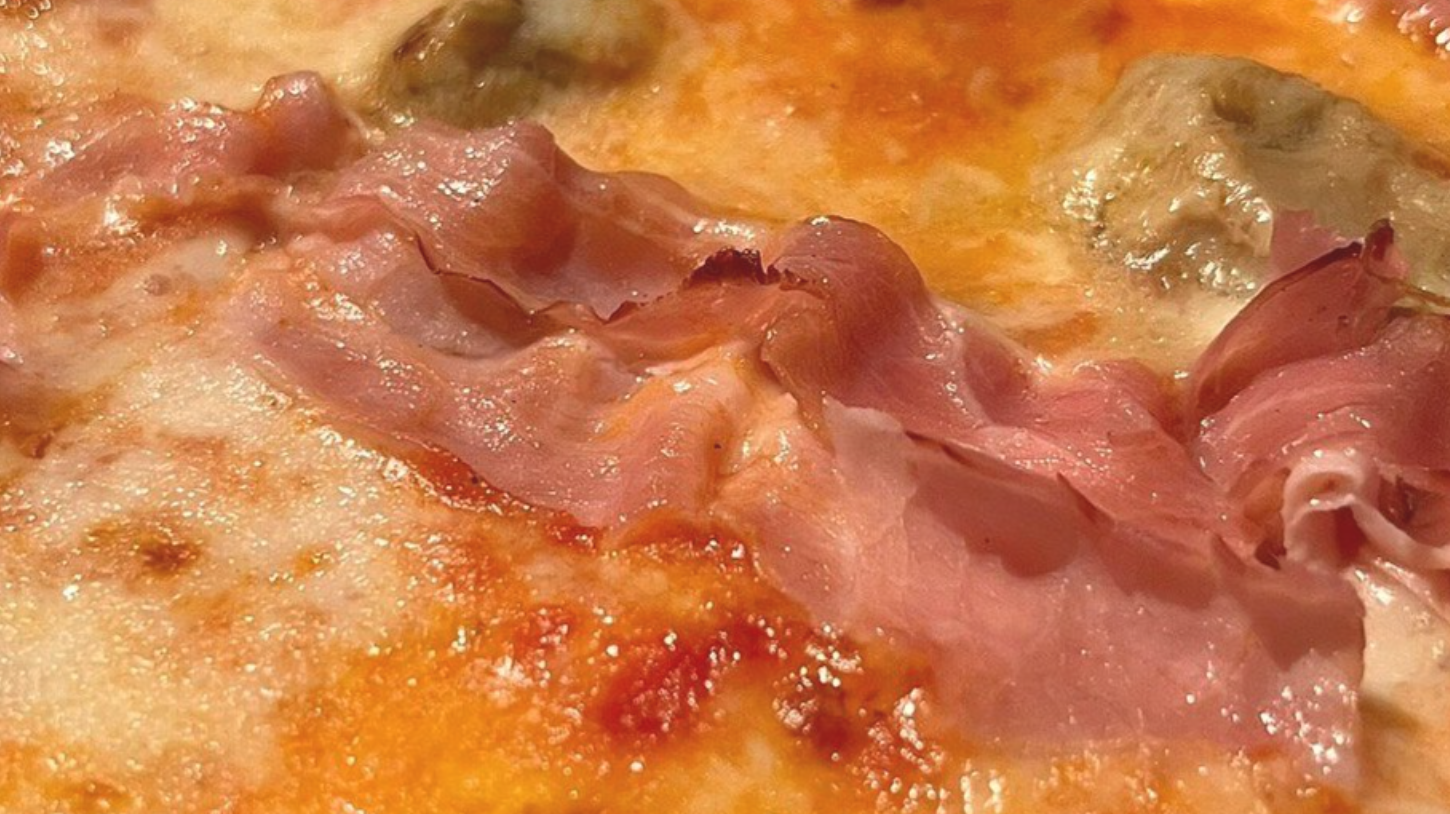 Primo piano di una pizza ricca di formaggio, guarnita con fette di prosciutto rosa piegate.