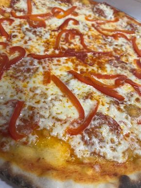 Primo piano di una pizza ricca di formaggio, guarnita con strisce di peperone rosso e crosta dorata.