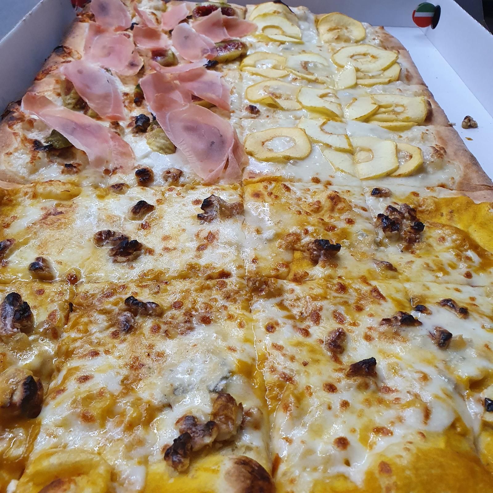 Fette di pizza assortite in scatola, con condimenti a base di prosciutto, pera e formaggio.