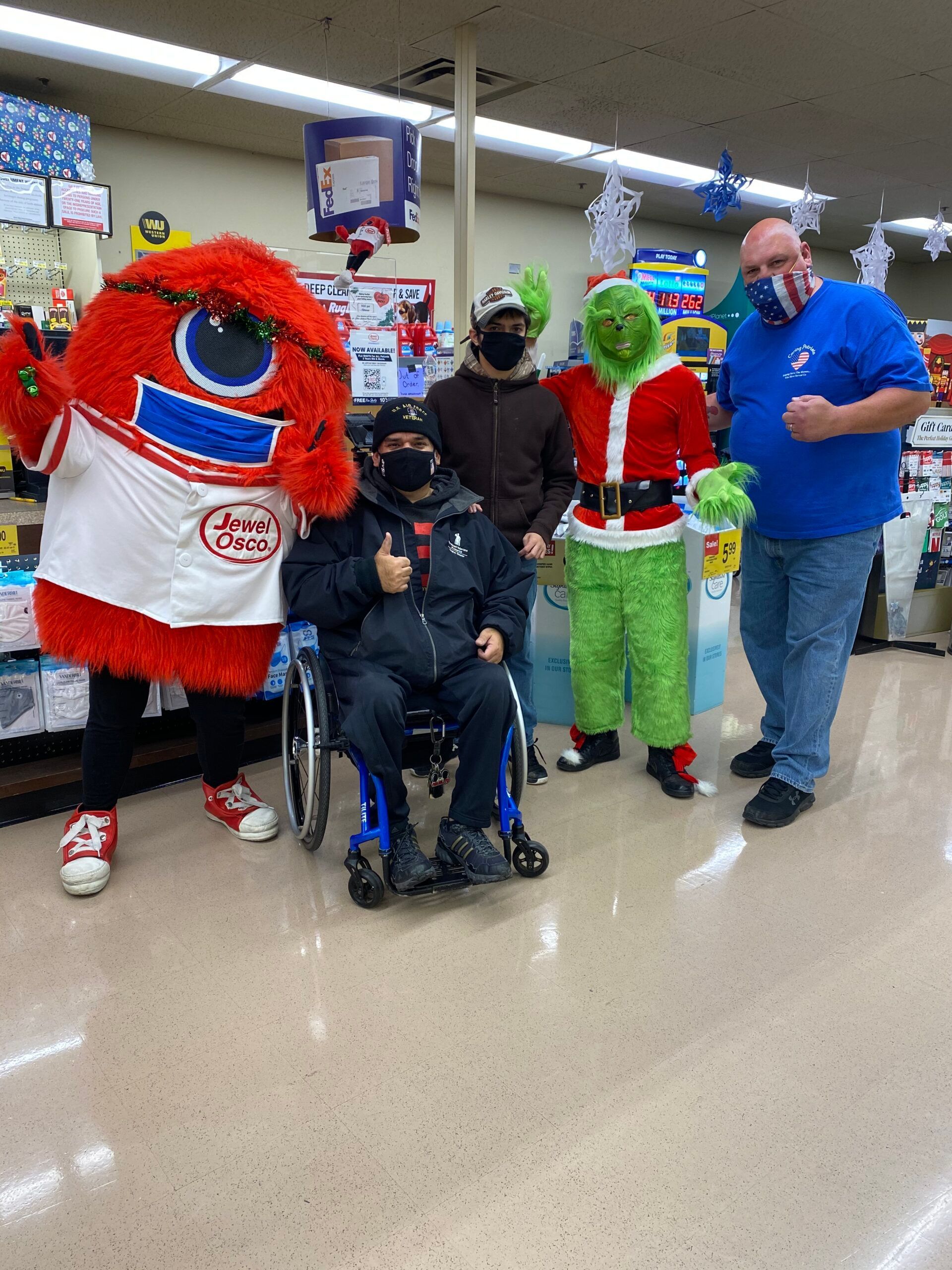 Costumed characters posing with a person in a wheelchair at a community event in a store.