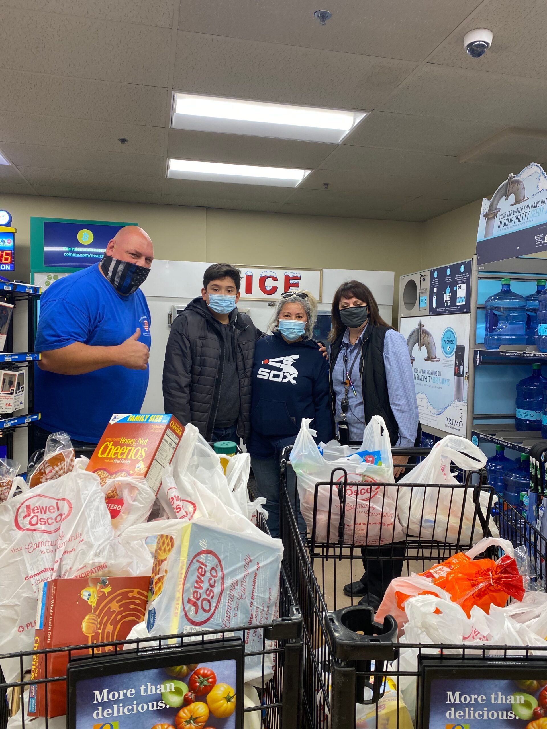 Three people posing in a grocery store behind carts filled with food and supplies.