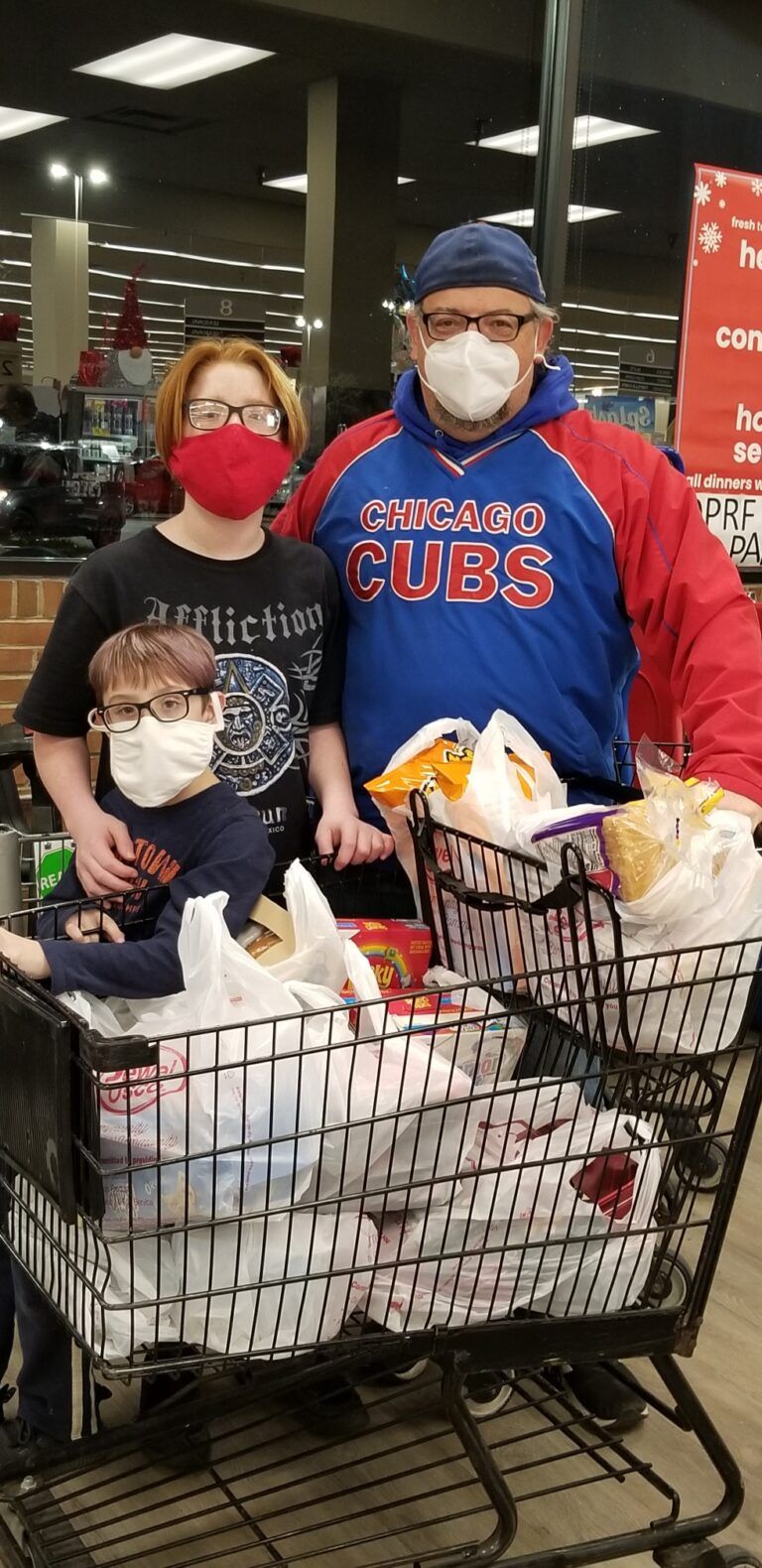 Two shoppers in masks stand behind a cart full of groceries at a store checkout area.