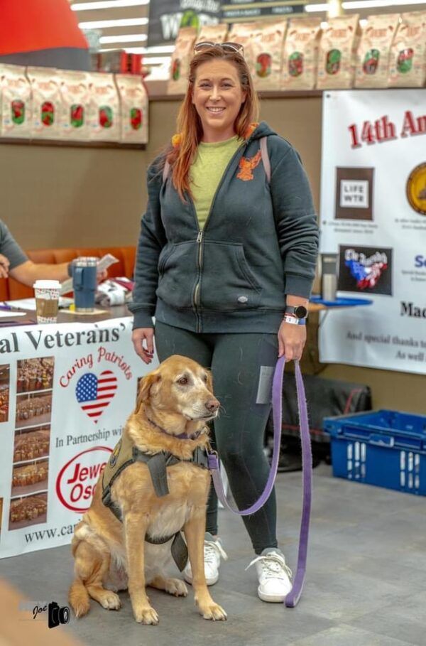 Woman standing with a golden retriever guide dog at an indoor event booth