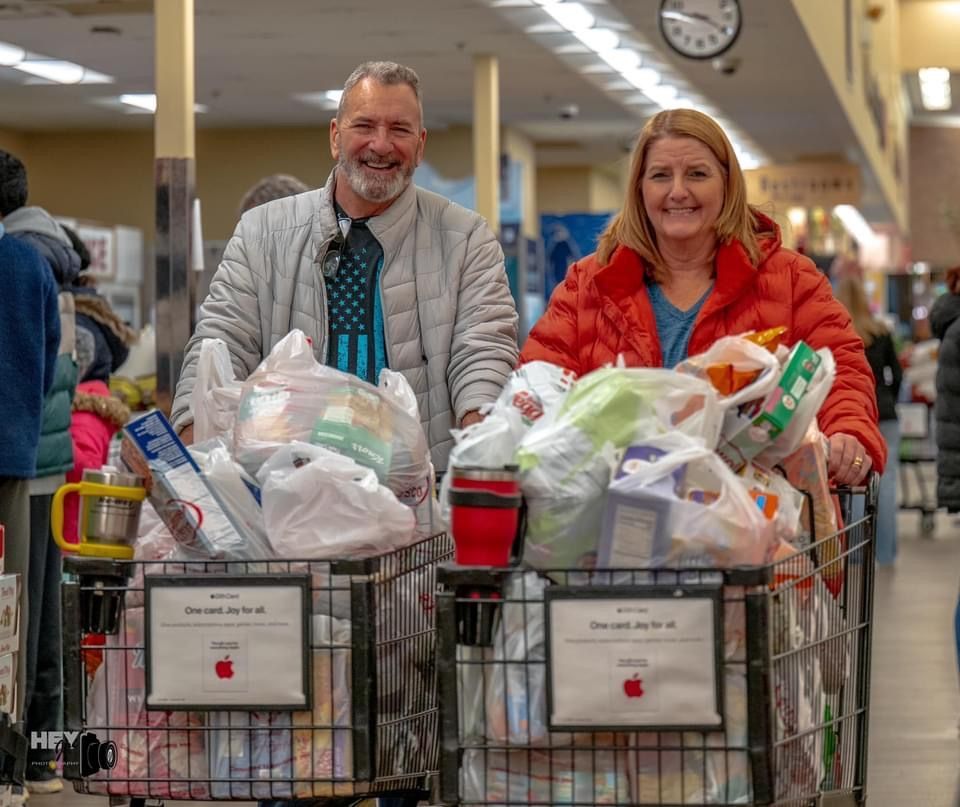 Two volunteers smile behind shopping carts full of donated goods in a store aisle.