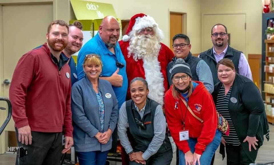 Group of smiling people posing indoors, with one person dressed as Santa Claus in the center.