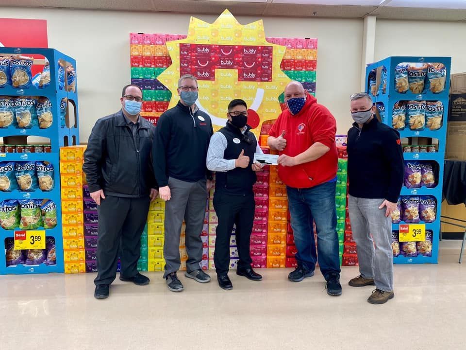 Five people standing in a store aisle, posing beside stacked colorful donation boxes and a red display sign