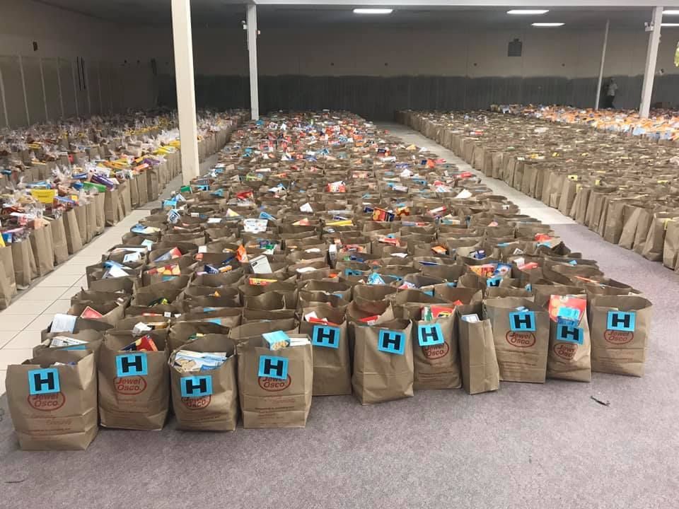Rows of brown grocery bags with blue labels lined up in a large warehouse-like room