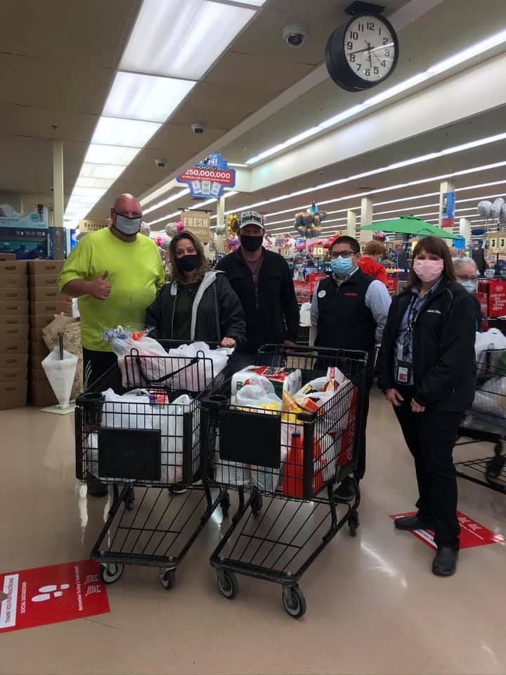 Shoppers standing with carts in a grocery store aisle, wearing face masks.