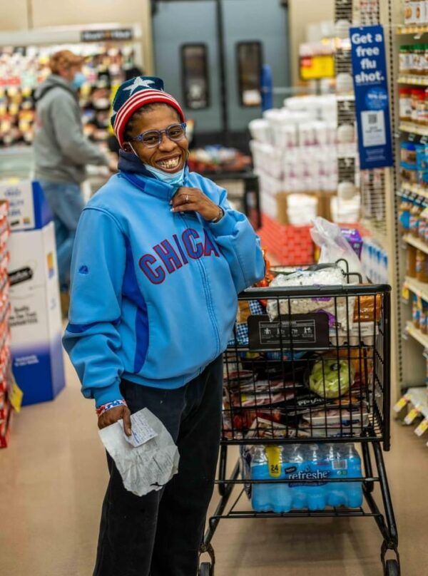 Smiling shopper in a blue Chicago sweatshirt stands beside a grocery cart in a store aisle.