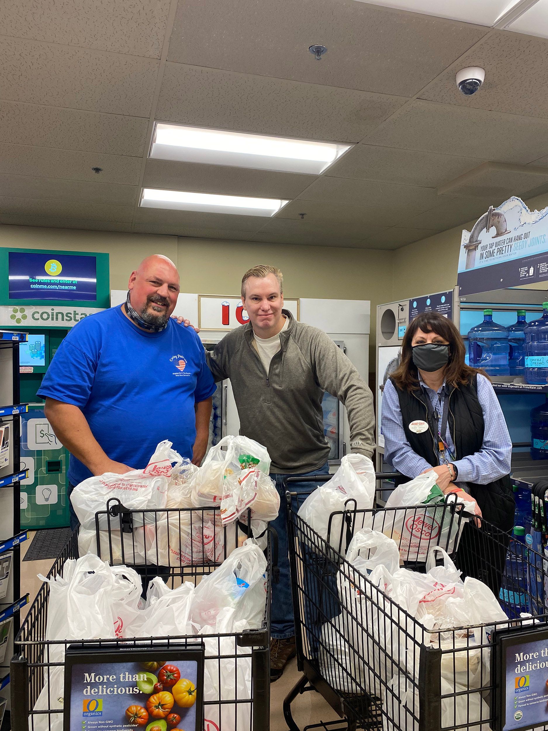 Three people stand behind carts full of donated groceries in a store aisle.