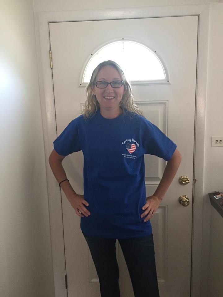 Woman standing indoors in a blue T-shirt and black pants, smiling with hands on hips.