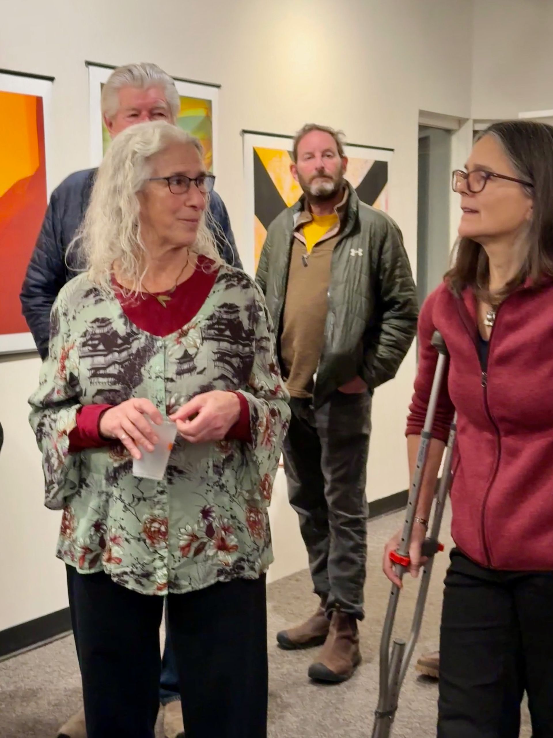 People standing in an art gallery, talking beside colorful abstract paintings.