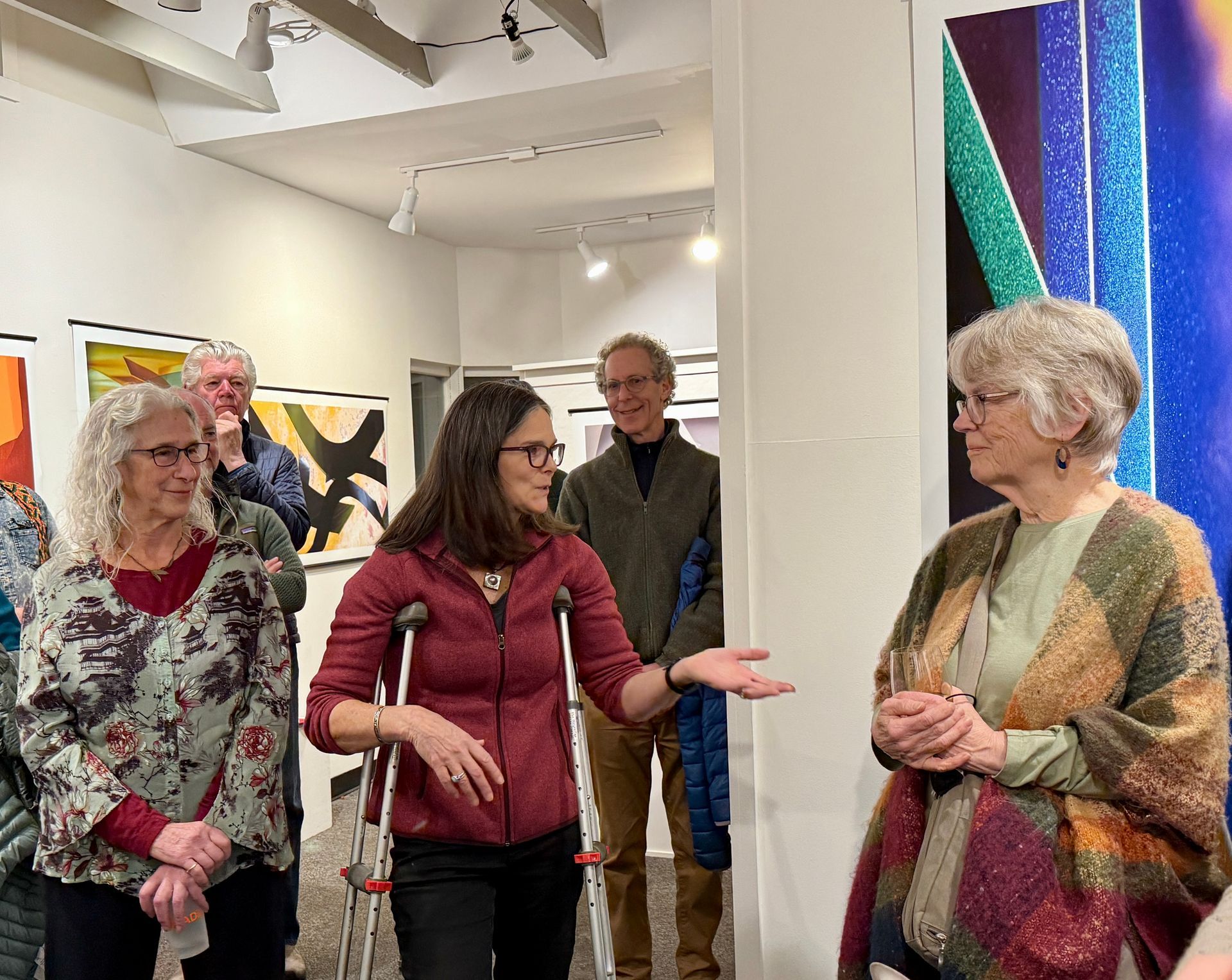 People gathered in an art gallery, one woman gesturing while speaking beside colorful wall art.