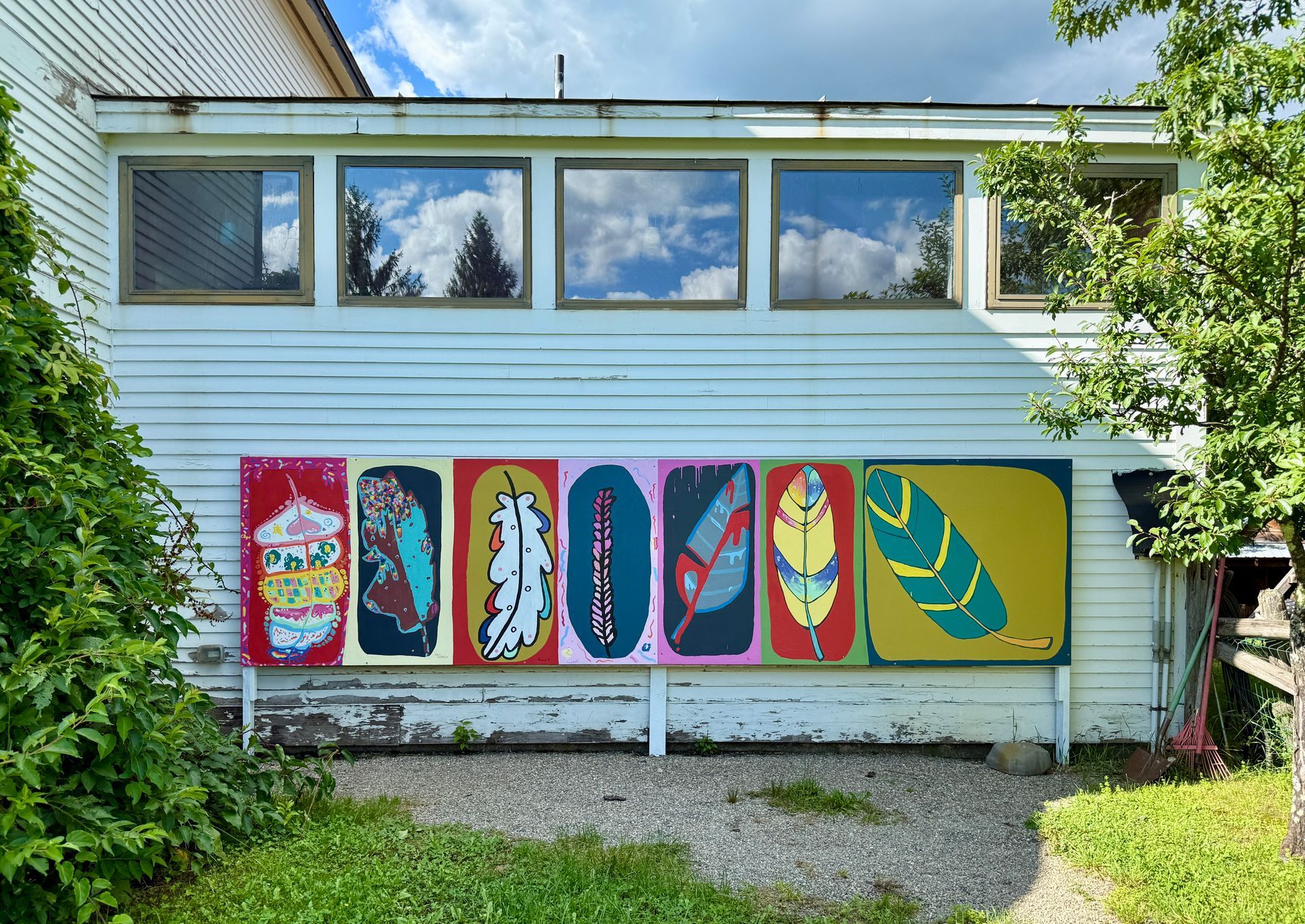 Colorful surfboard mural on a building wall beneath windows and trees