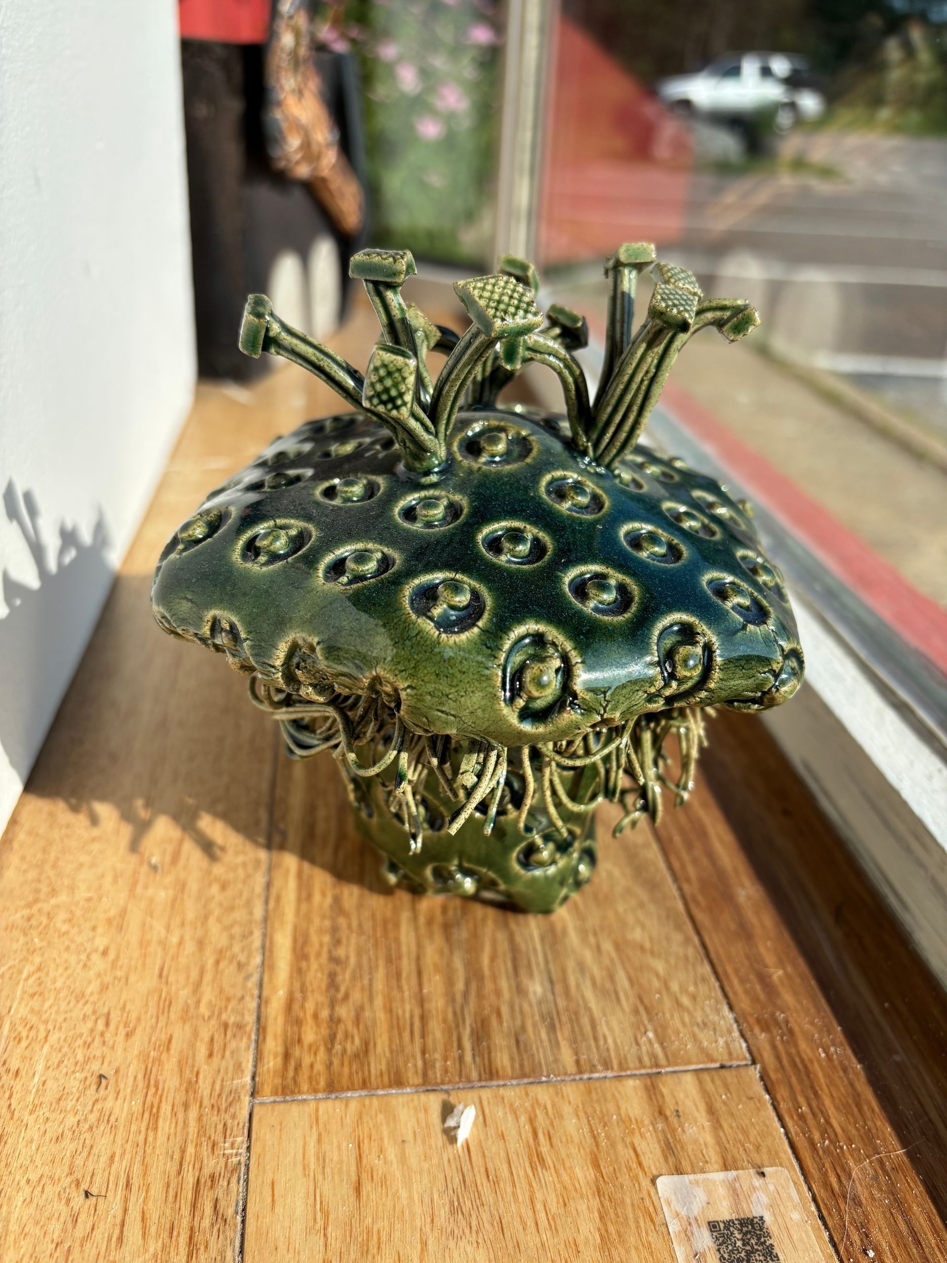 Small green ceramic mushroom ornament with ringed spots, sitting on a wooden windowsill.