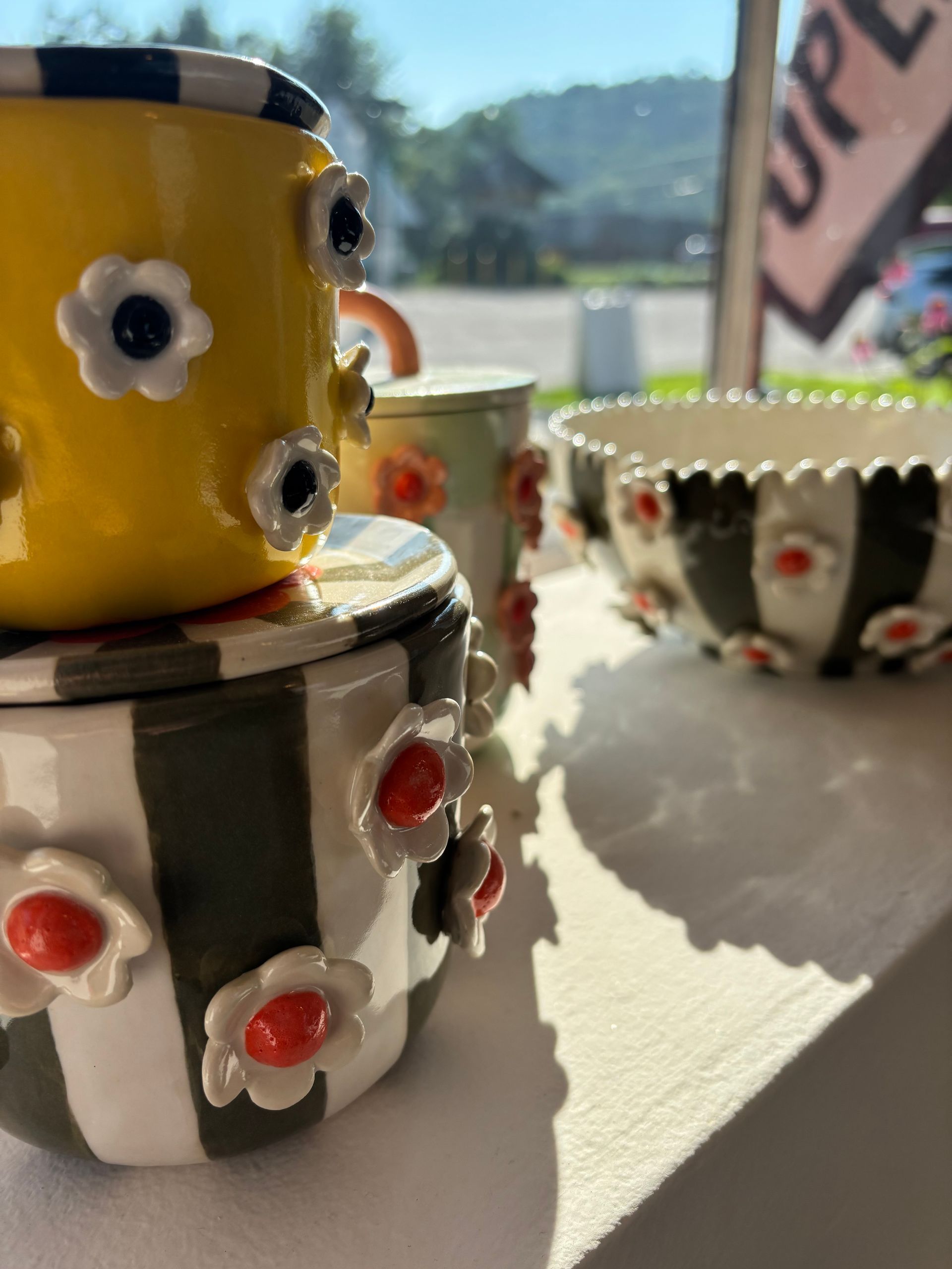 Colorful painted ceramic cups and bowls on a sunny windowsill