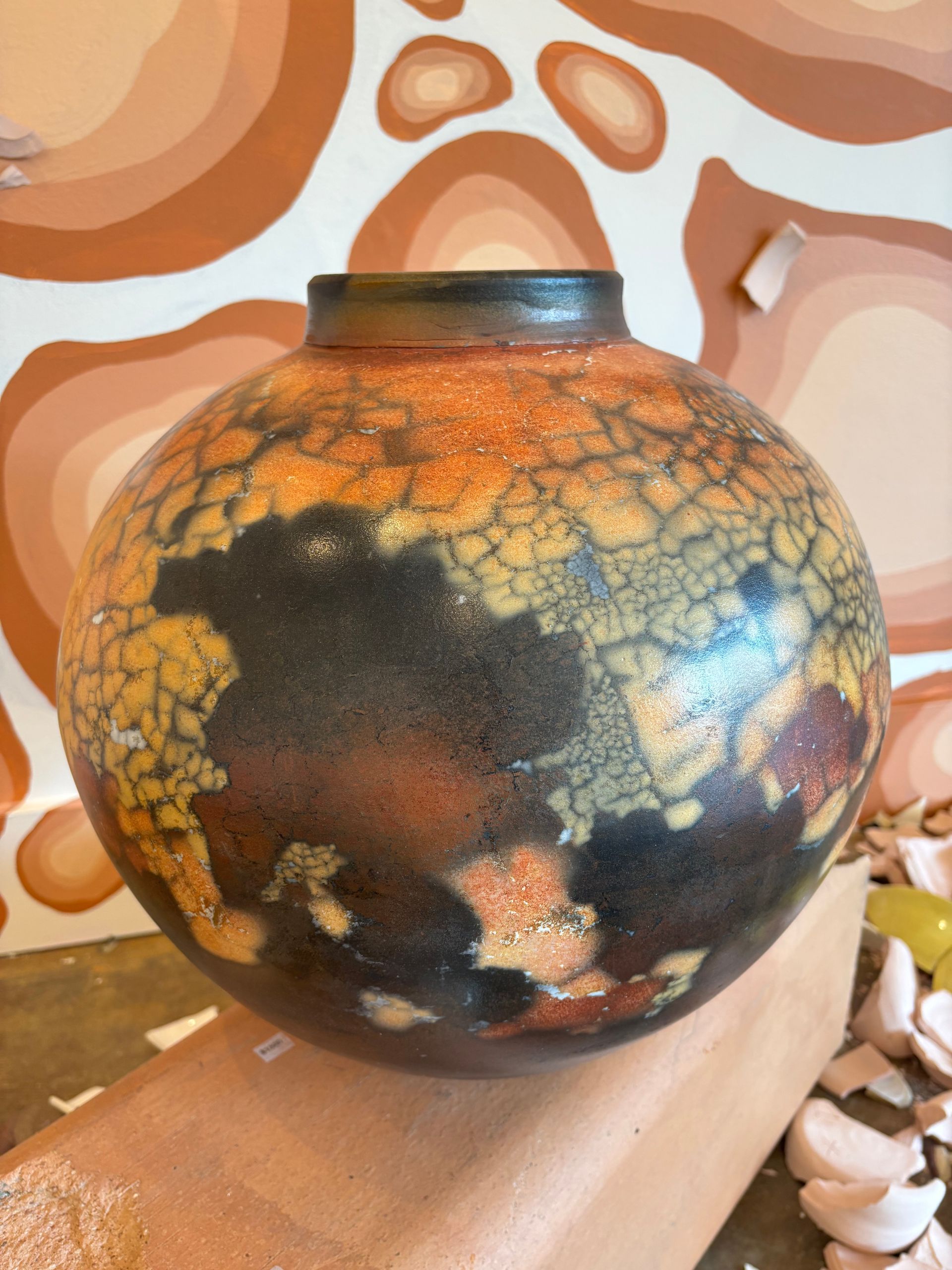 Round decorative vase with black, orange, and blue crackled glaze on a wooden shelf