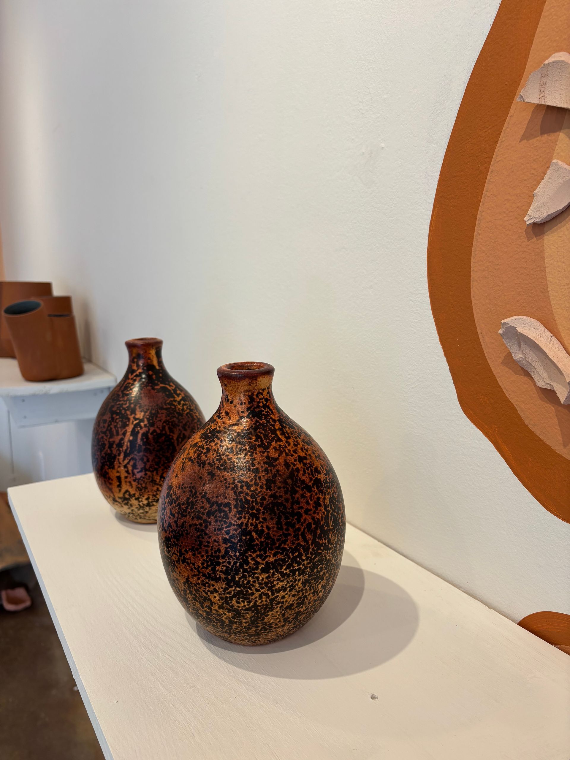 Two speckled brown ceramic vases on a white shelf beside a wall art piece