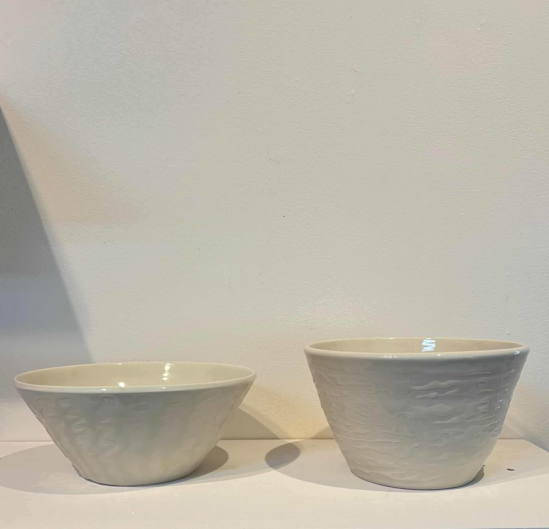 Two small light gray ceramic bowls on a white shelf against a plain wall