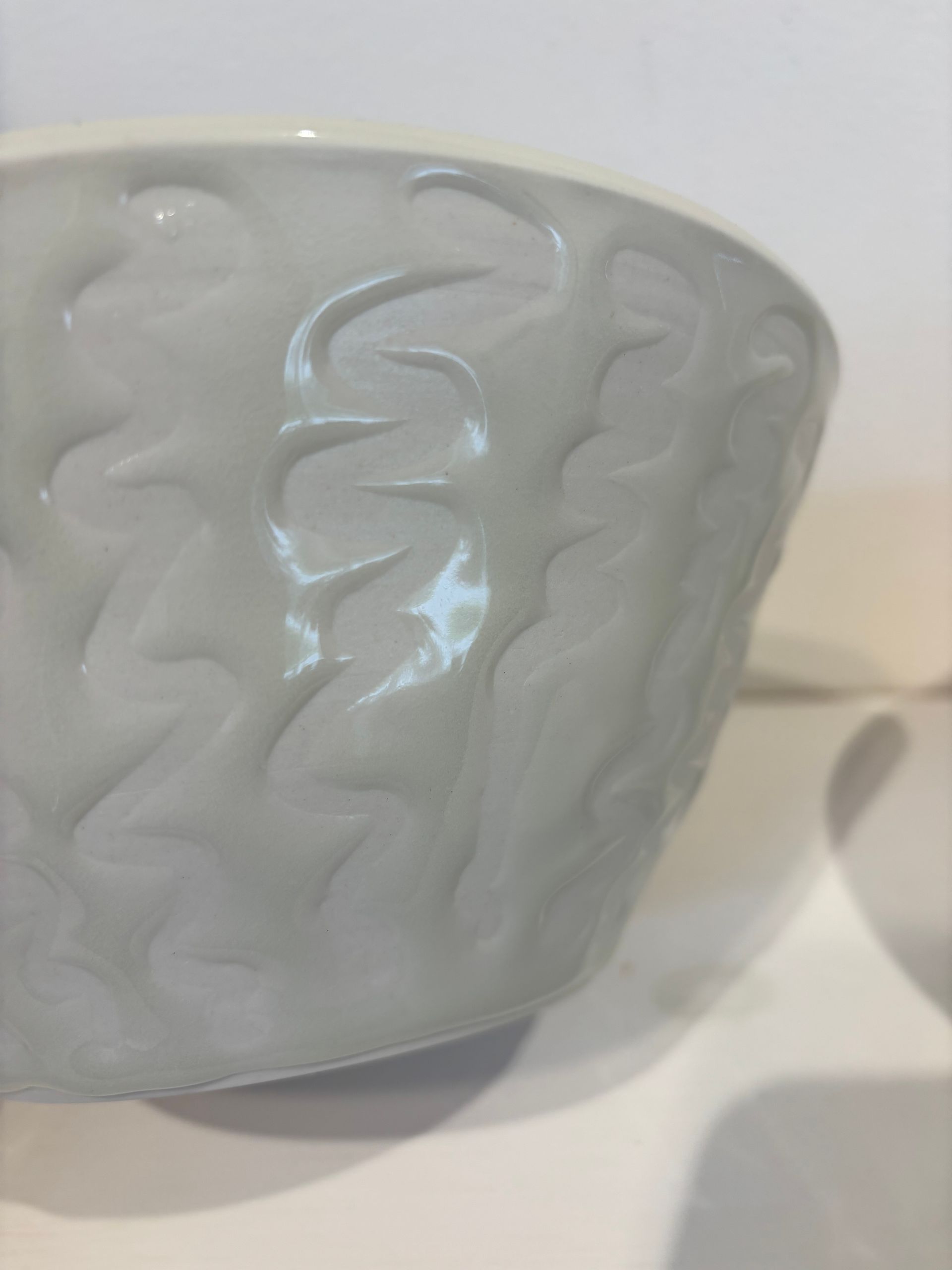 Close-up of a white ceramic bowl with embossed wavy patterns on a light surface.
