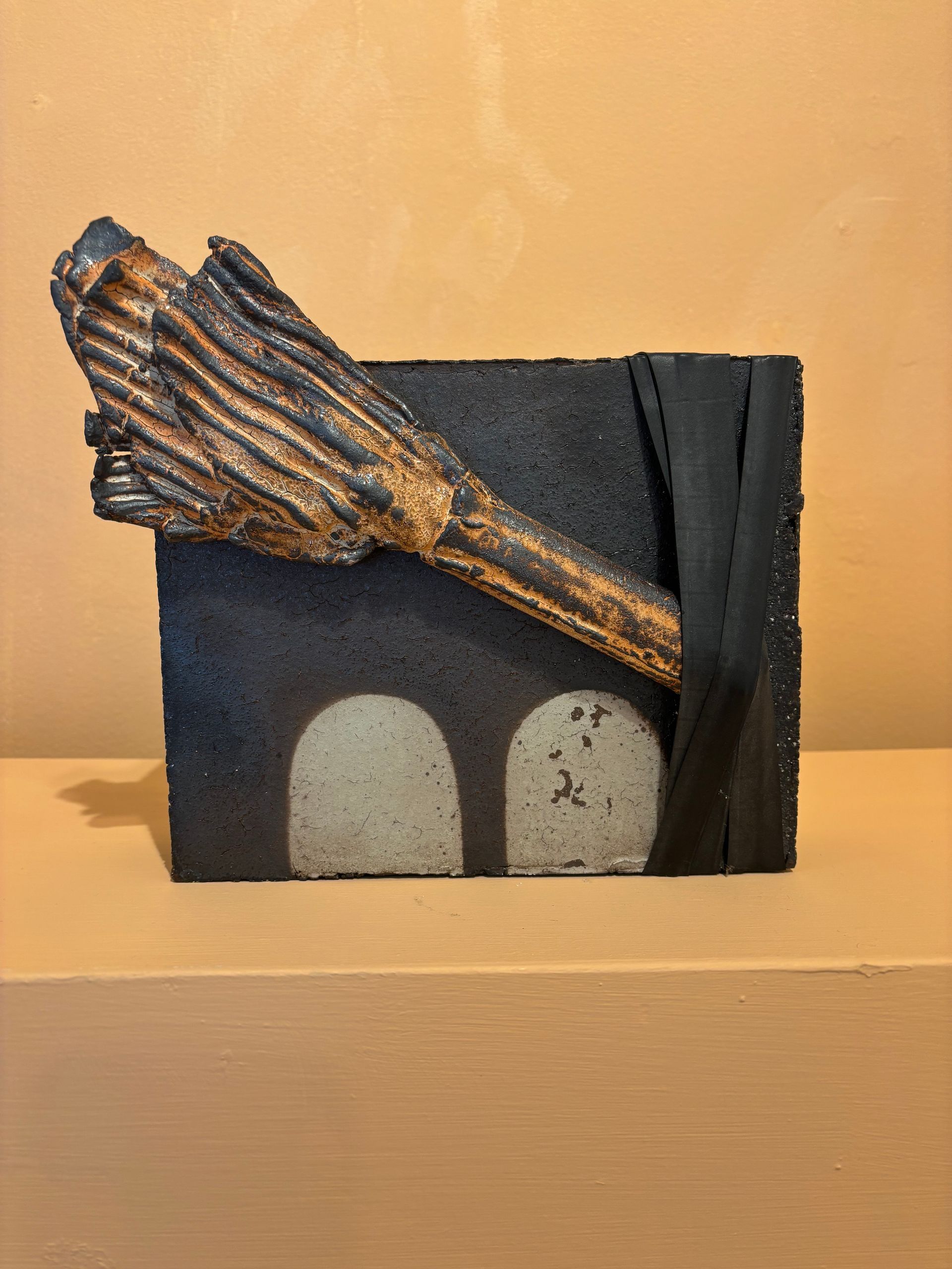Abstract sculpture with a textured black base and a bronze, wing-like form against a beige wall.