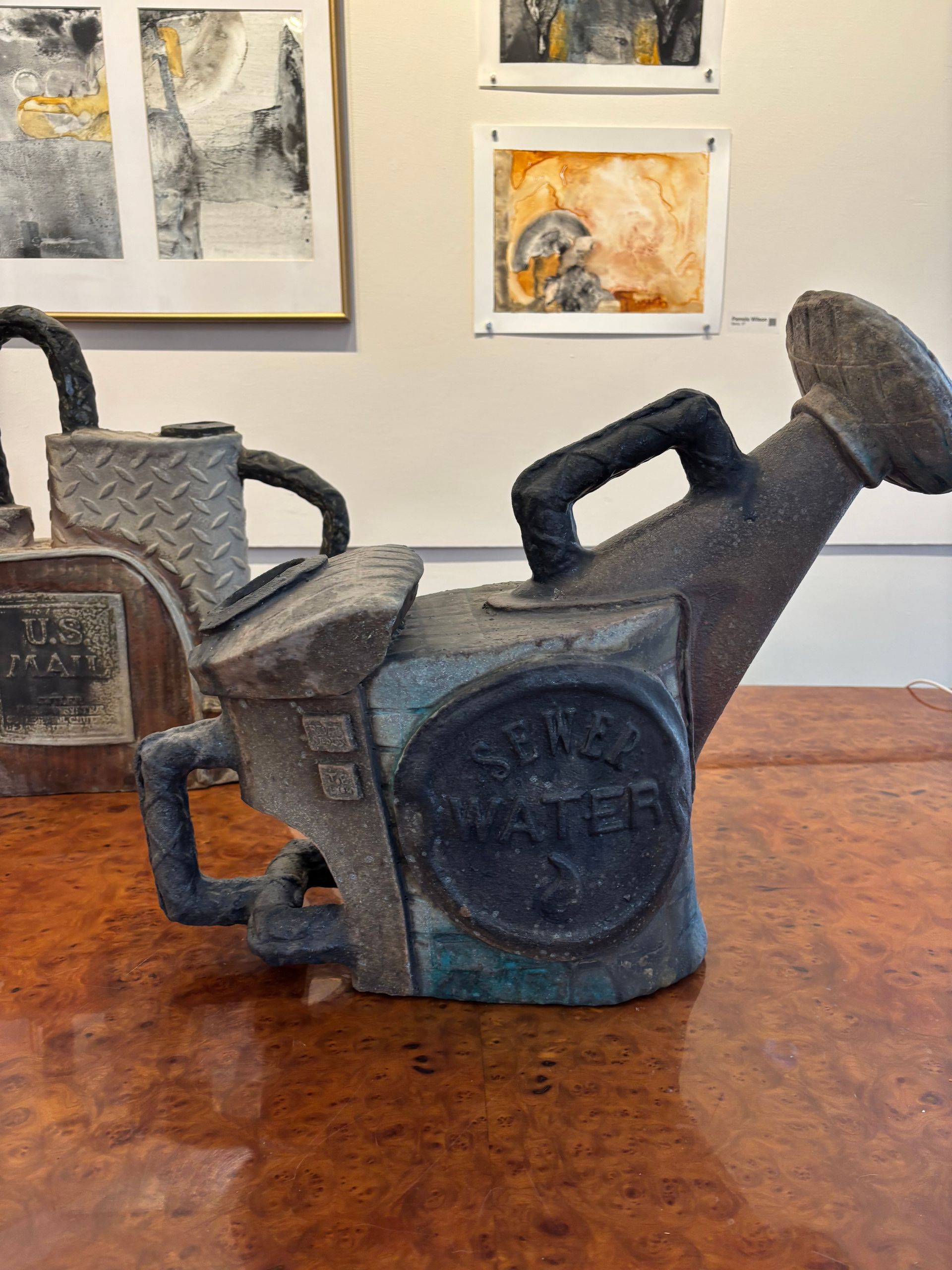Two dark metal sculptural chairs on a wooden table in an art gallery