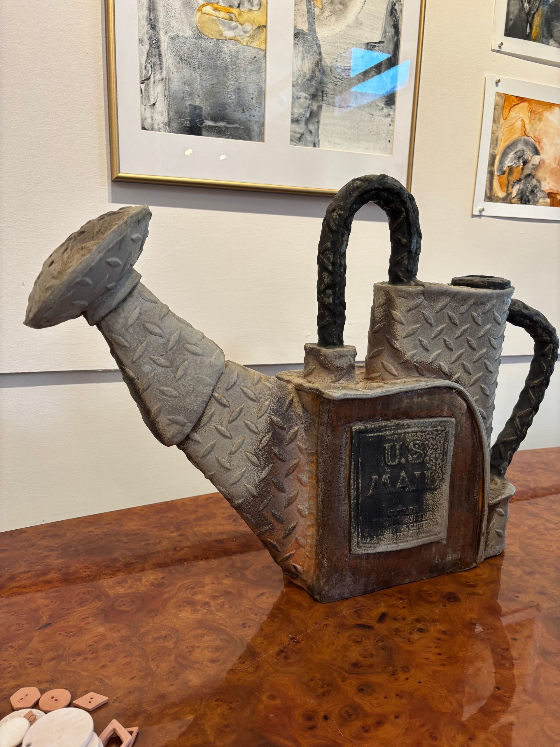 Rusty metal watering can sculpture with a black handle on a wooden table indoors