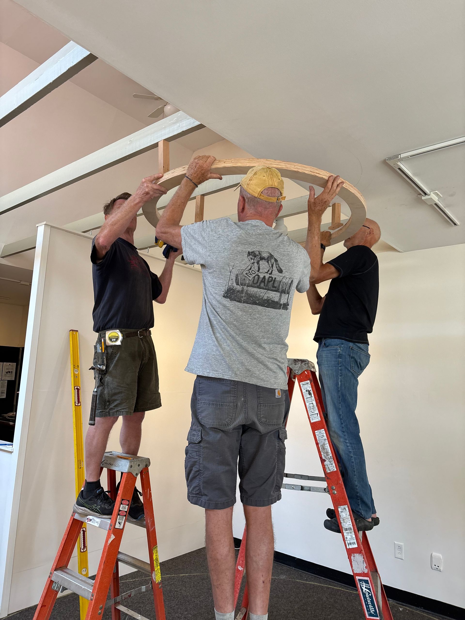 Three people on ladders lifting a wooden arch frame in a room under construction