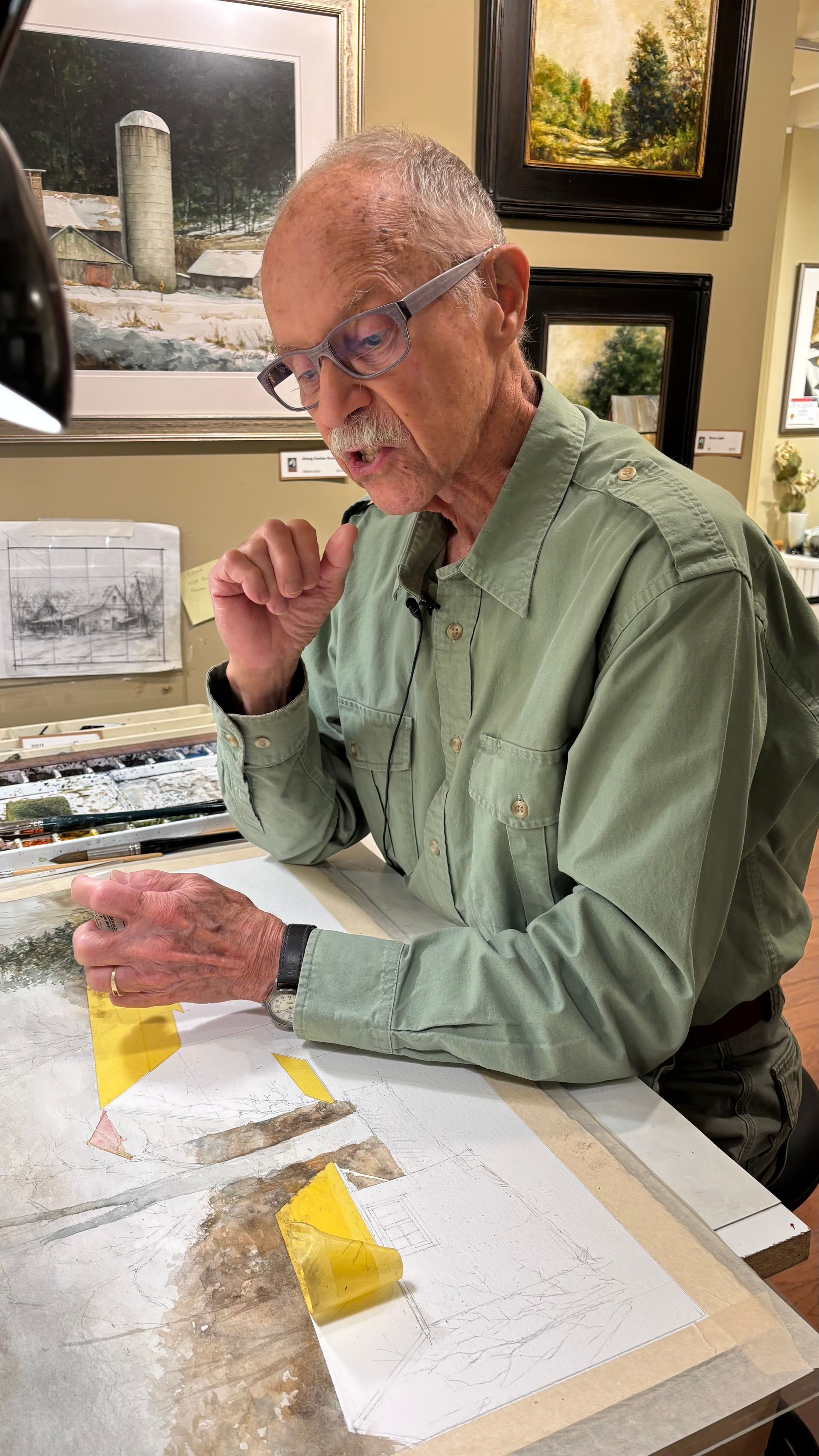 Man painting at a studio table, focused on a yellow-and-white abstract artwork.