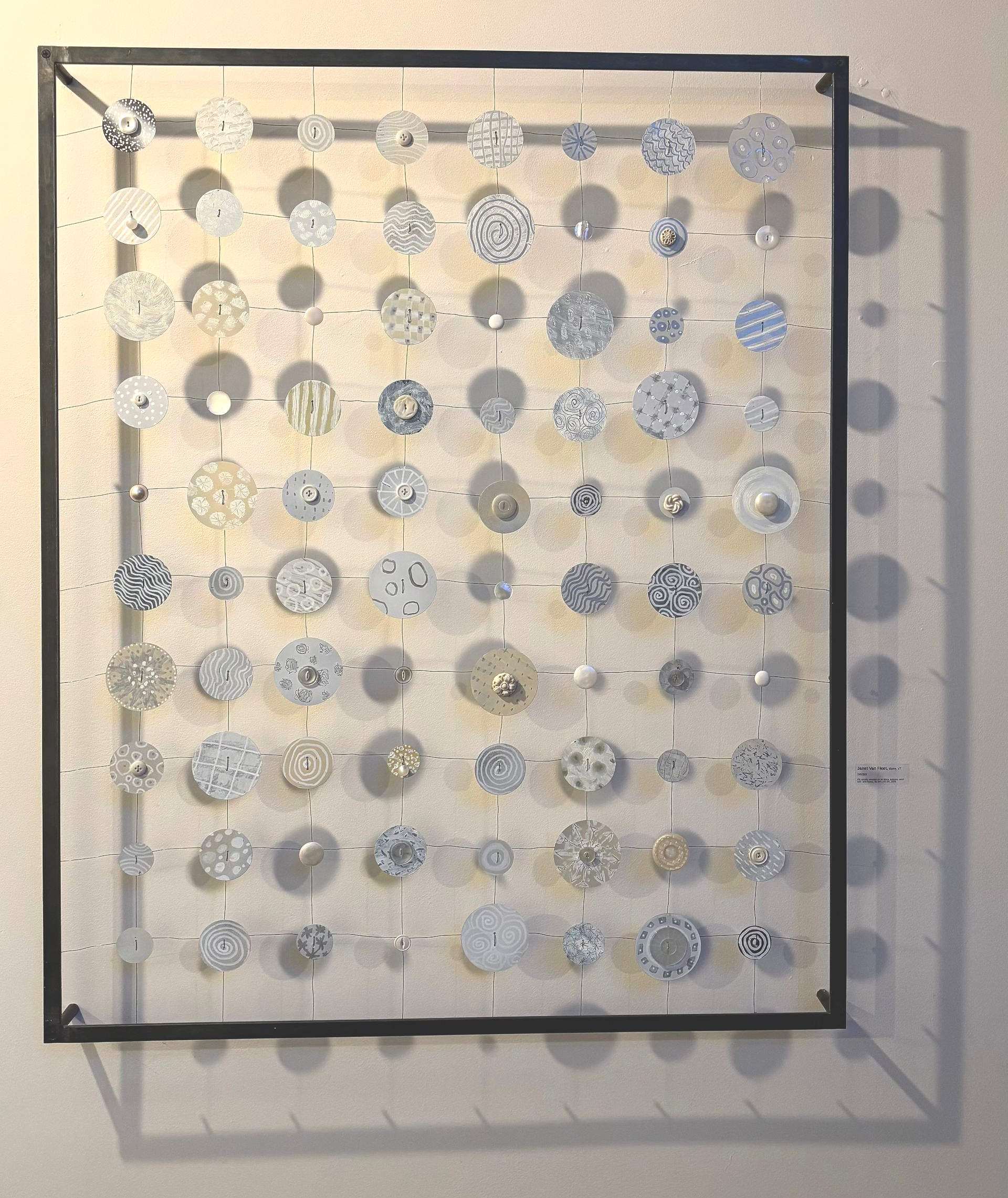 Abstract wall art of hanging clear discs in a black frame, casting shadows on a beige wall