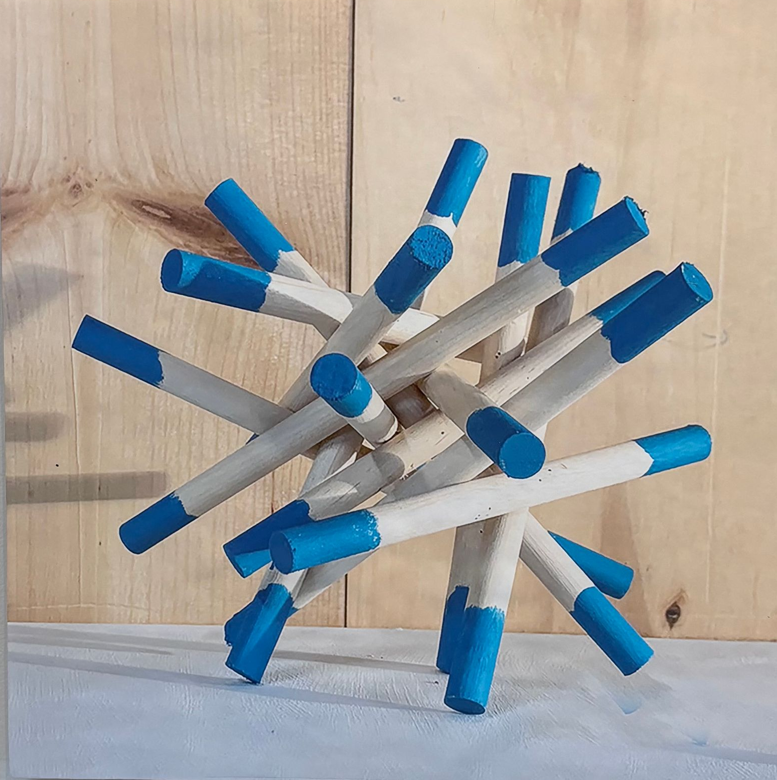 Abstract sculpture of intersecting white rods with blue tips on a light wood surface.