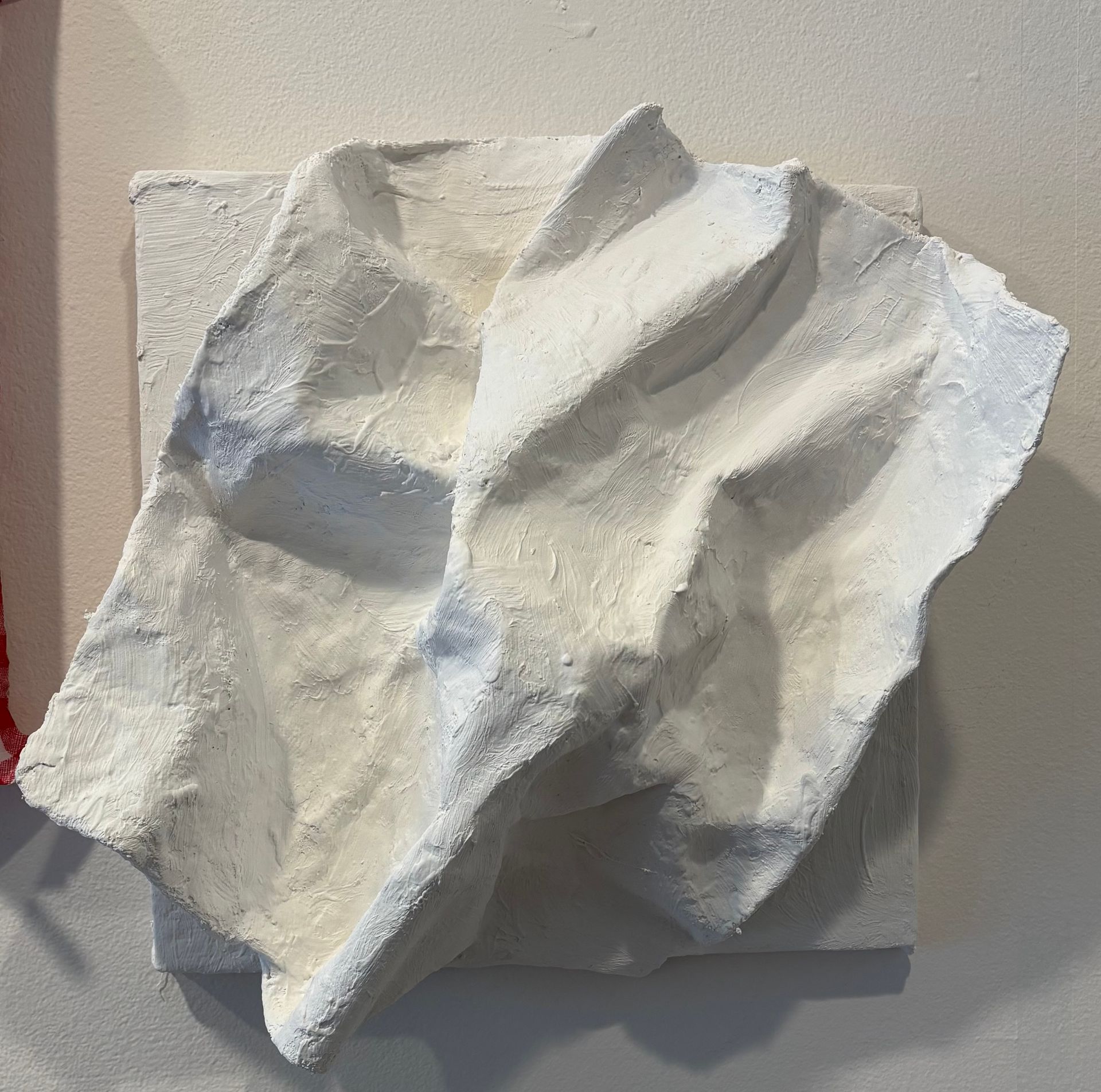 Abstract white folded paper sculpture mounted on a beige wall
