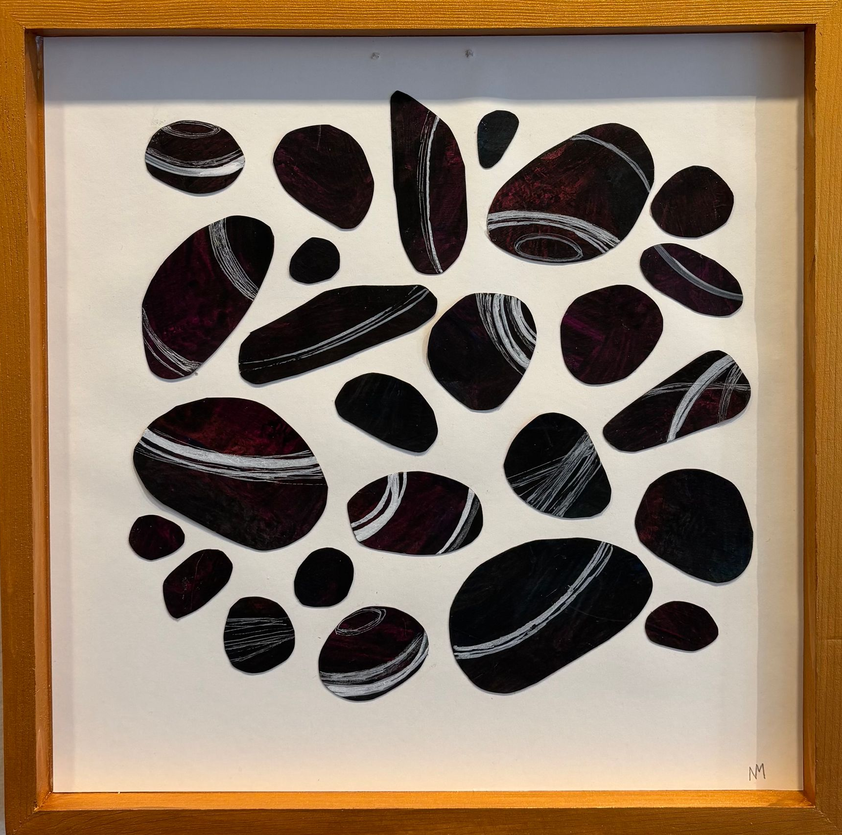 Framed abstract collage of black and burgundy pebble shapes on a white background
