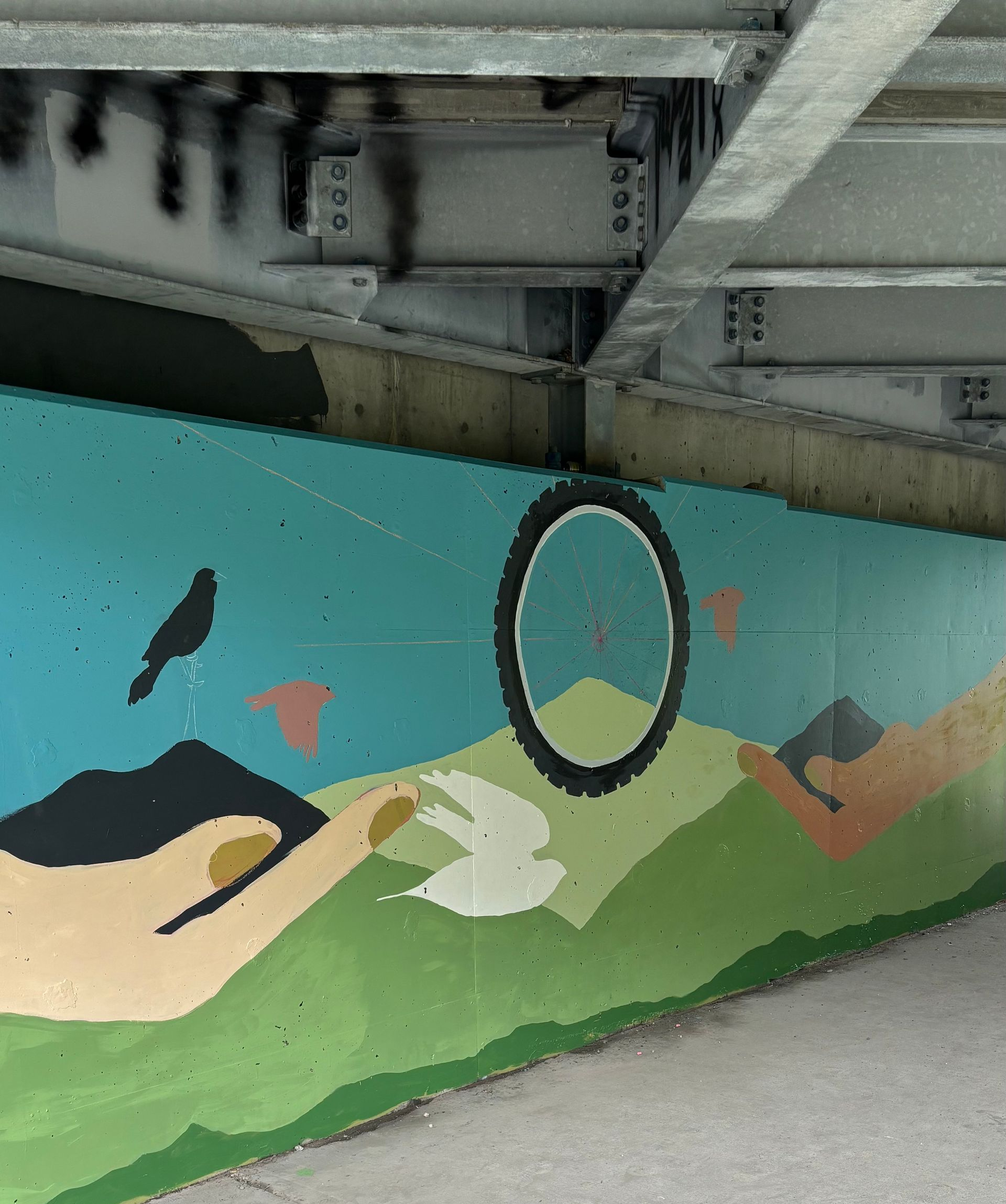Snowy underpass beneath a bridge with graffiti on concrete supports and a low waterway nearby