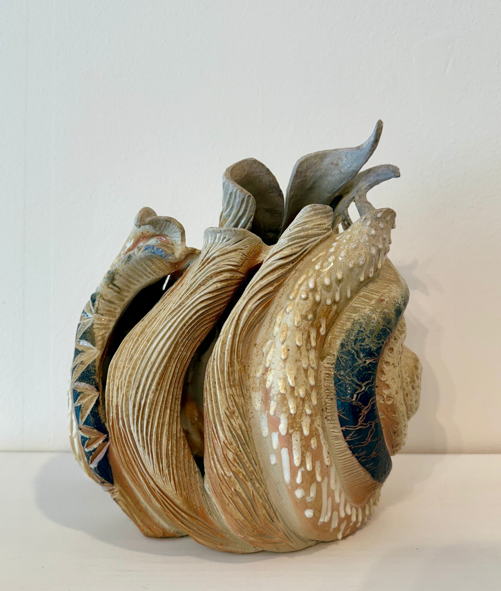 A beige and blue seashell sculpture with layered, curved ridges on a white surface