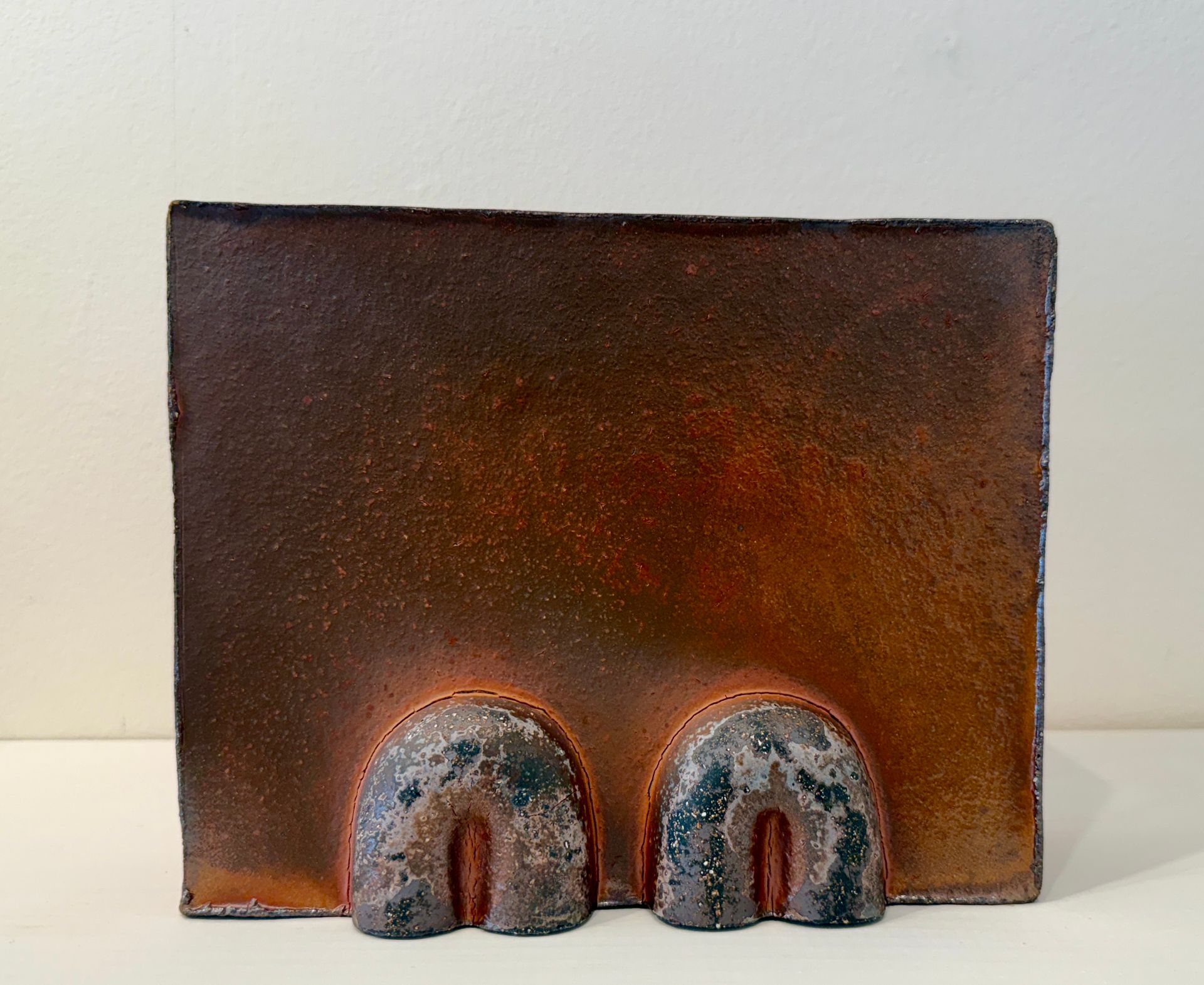 Rustic brown ceramic plaque with two small arched openings at the bottom