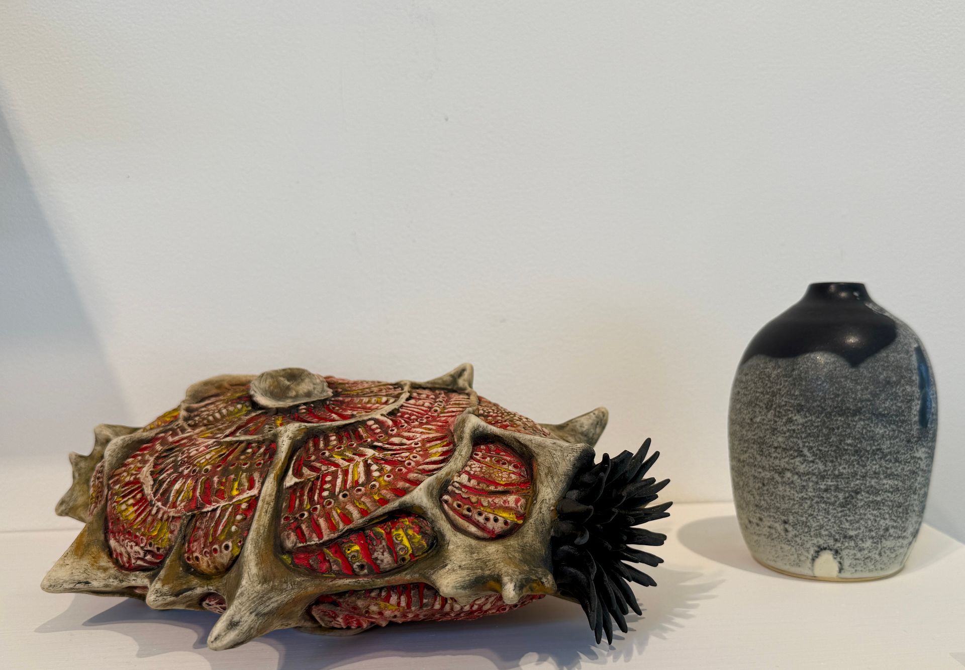 Two decorative ceramic sea urchin sculptures, one colorful and one gray, on a white surface