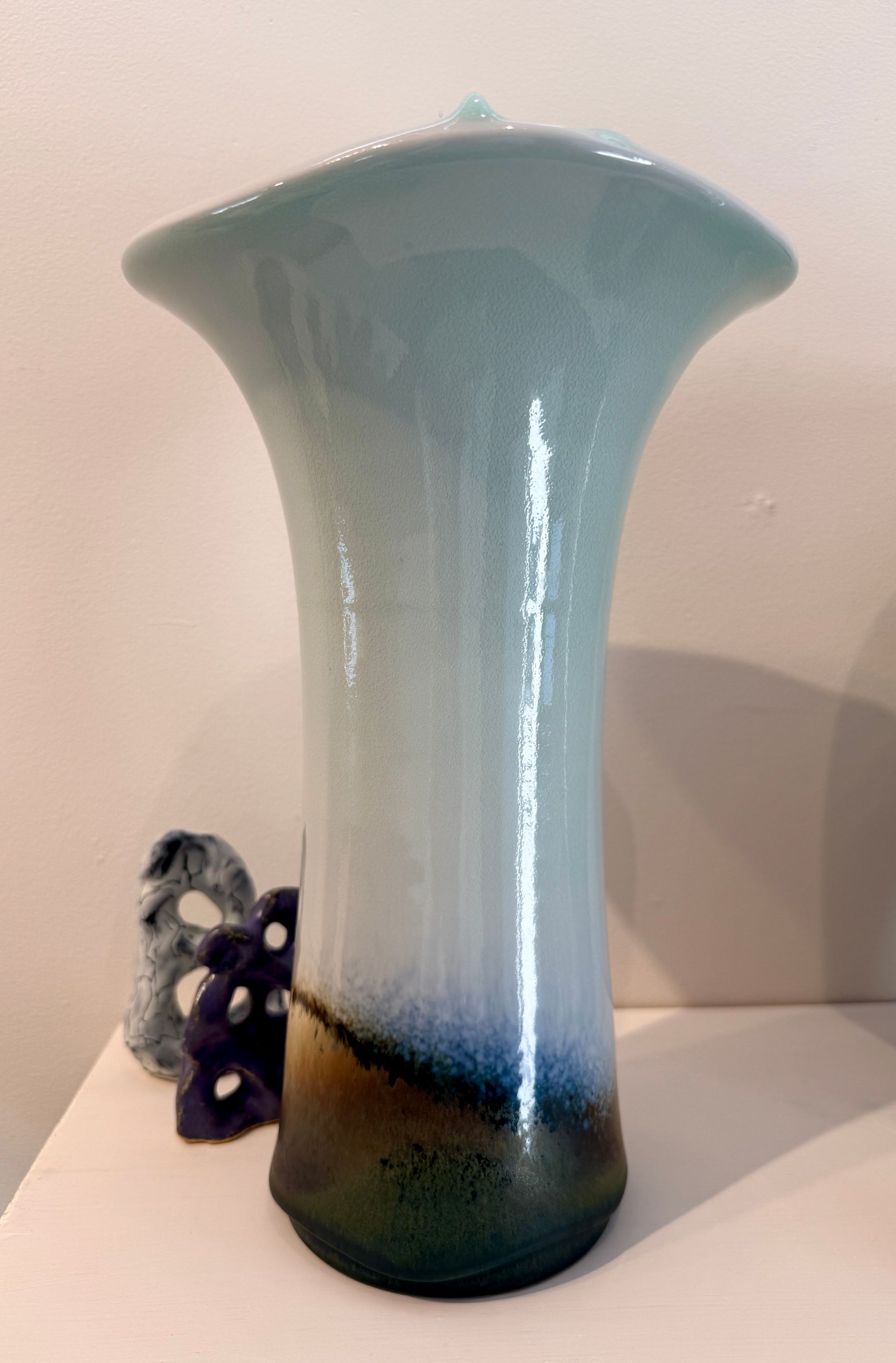 Tall iridescent blue-green vase with a flared rim on a light surface