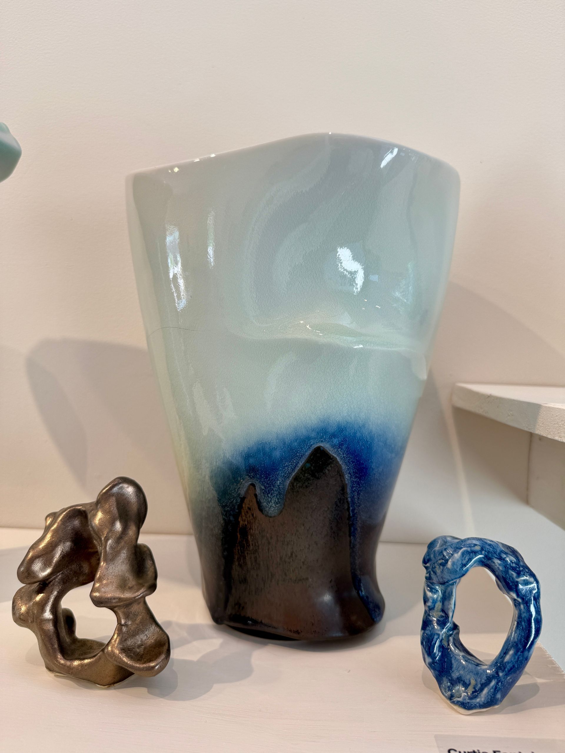 Three decorative glass sculptures on a shelf, including a tall blue vase and two small abstract pieces.