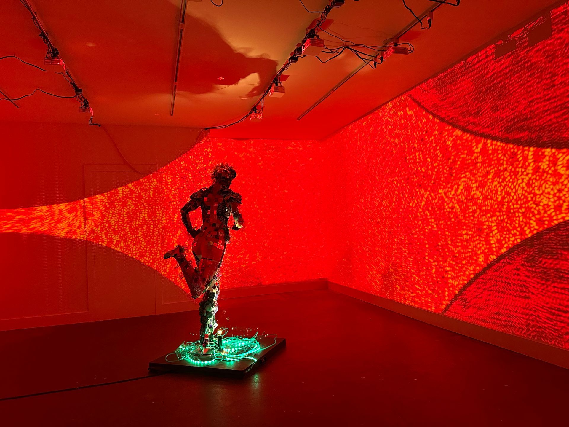 A dark sculpture on a glowing green base in a red-lit gallery with a curved wall display