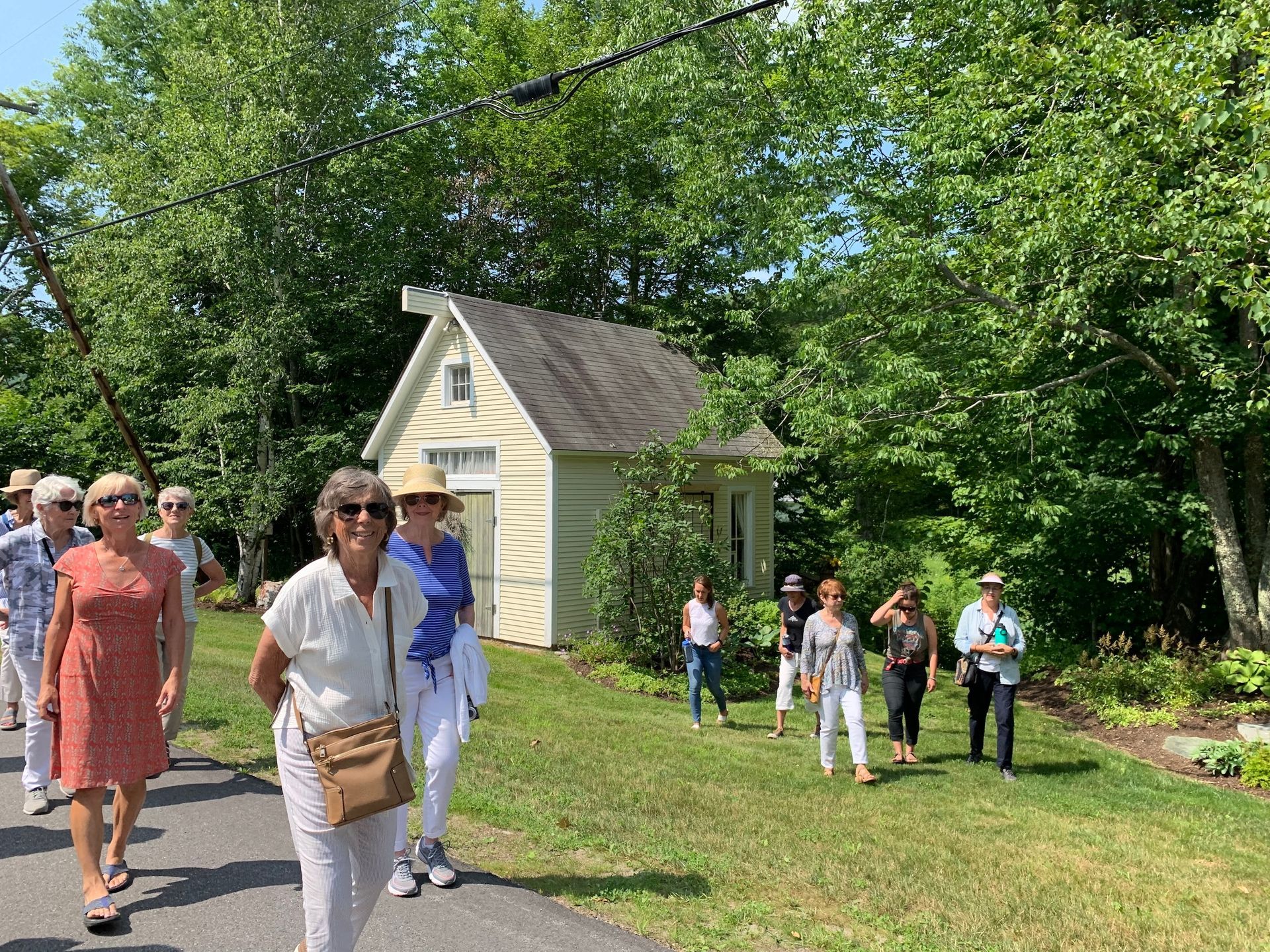 People walking on a garden path beside a small white shed in a sunny park