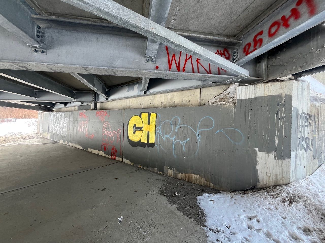 Graffiti-covered concrete underpass with yellow “CH” on a gray wall and snow at the edge