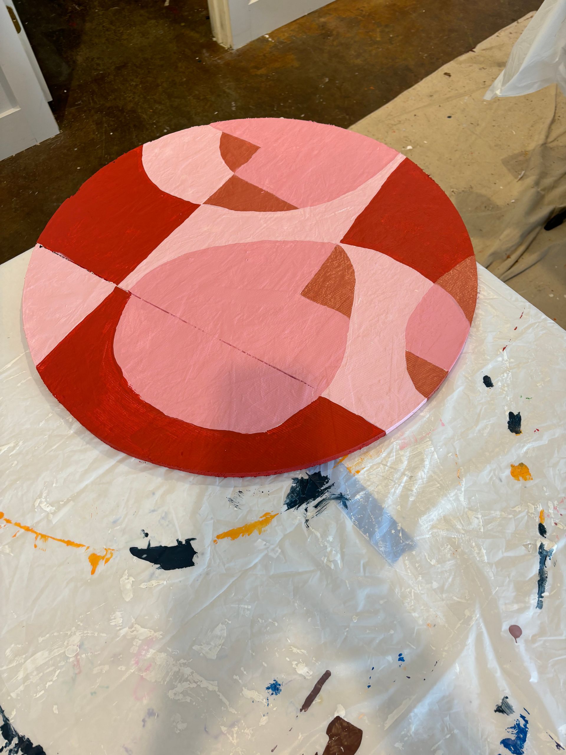 Abstract pink and red circular painted design on a canvas floor covering in an art studio