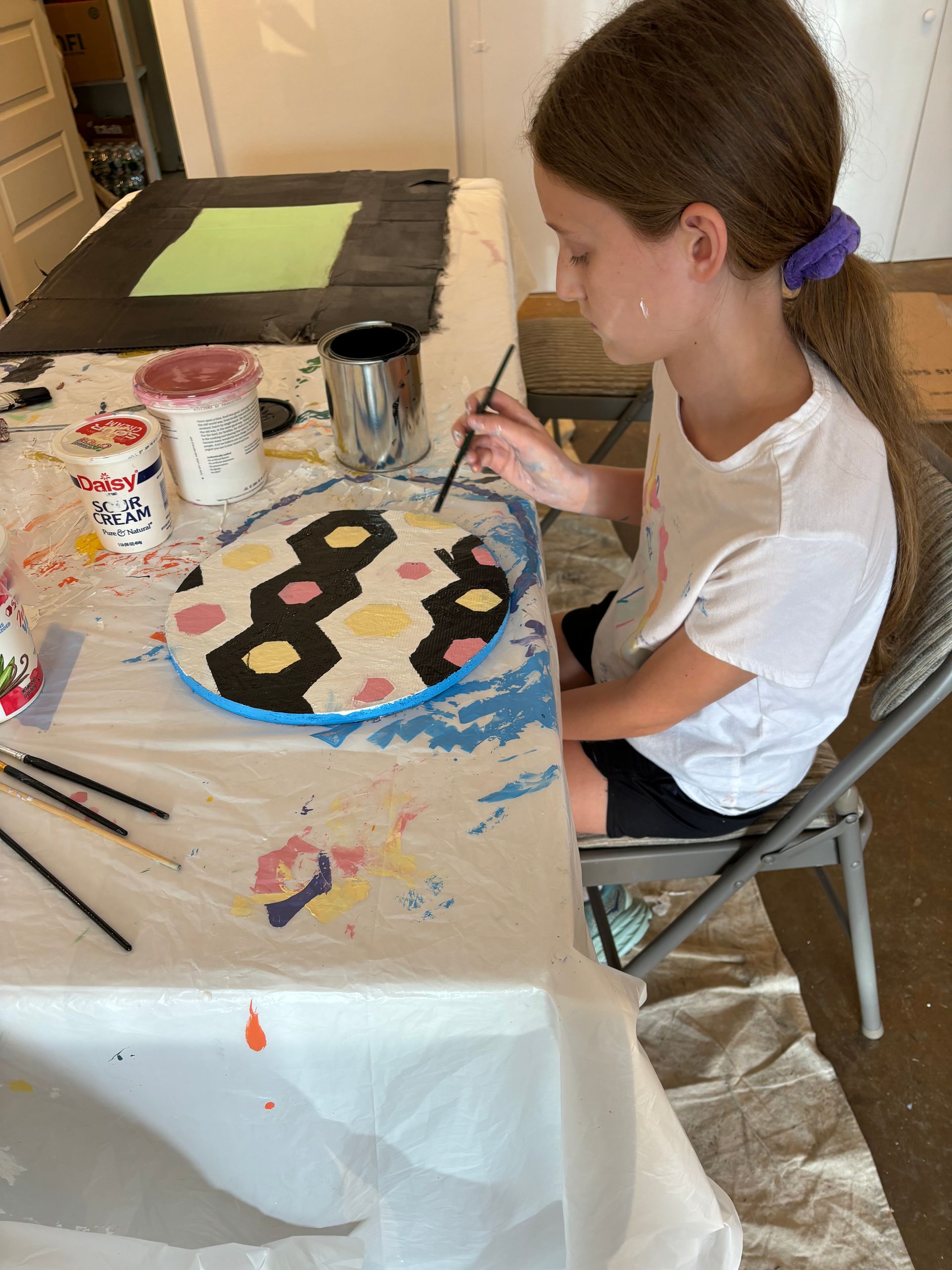 Person painting a colorful craft at a table with paint, brushes, and art supplies