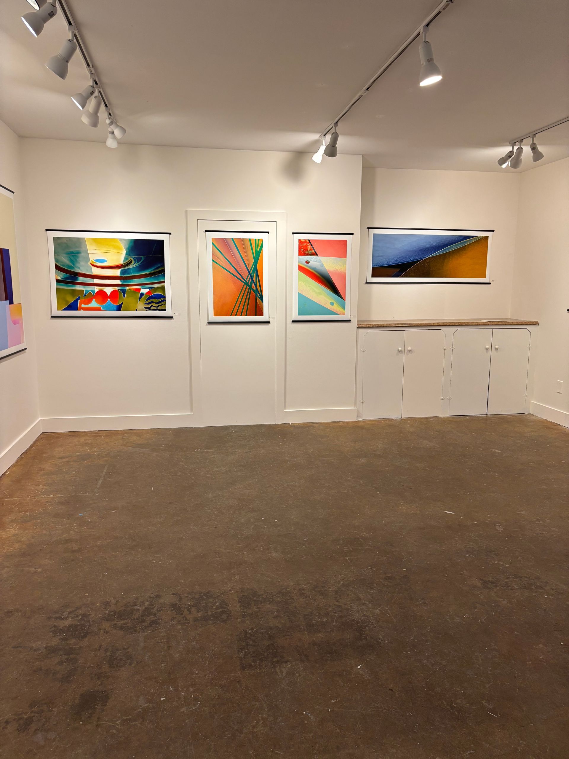 Art gallery with colorful abstract paintings on white walls under track lighting